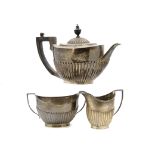 An Edwardian silver three piece tea set from Goldsmiths & Silversmiths, helmet shaped with fluted