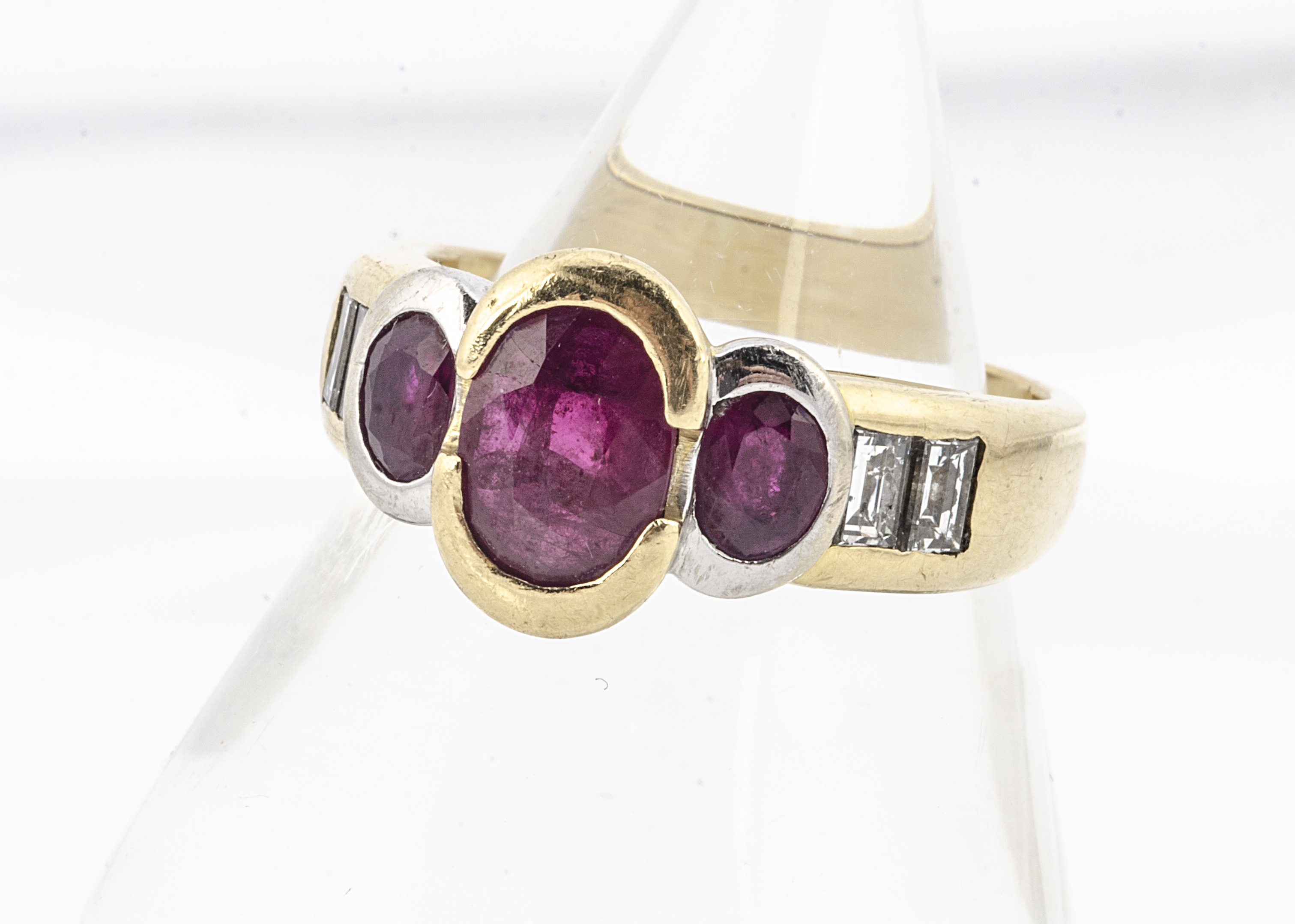 An 18ct gold three stone ruby and diamond set dress ring, the three oval cut rubies in rubbed over