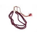 A ruby three strand bead necklace, each semi opaque bead being 8.3mm diameter, on red silk and