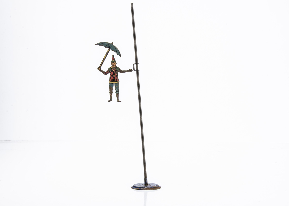 A Pre-War German Clown Gravity Toy, lithographed steel clown holding umbrella, attached to pole