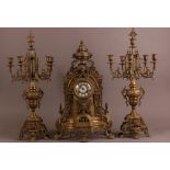 An early 20th century French brass clock garniture, having a pair of five branch candelabra with