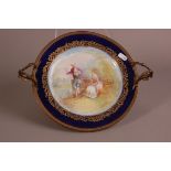 An early 20th century Sevres porcelain plate, mounted in a gilt stand with twin handles, 33cm