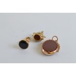 A gold swivel fob, in carnelian and bloodstone, another fob in black onyx and a triple tiger eye,