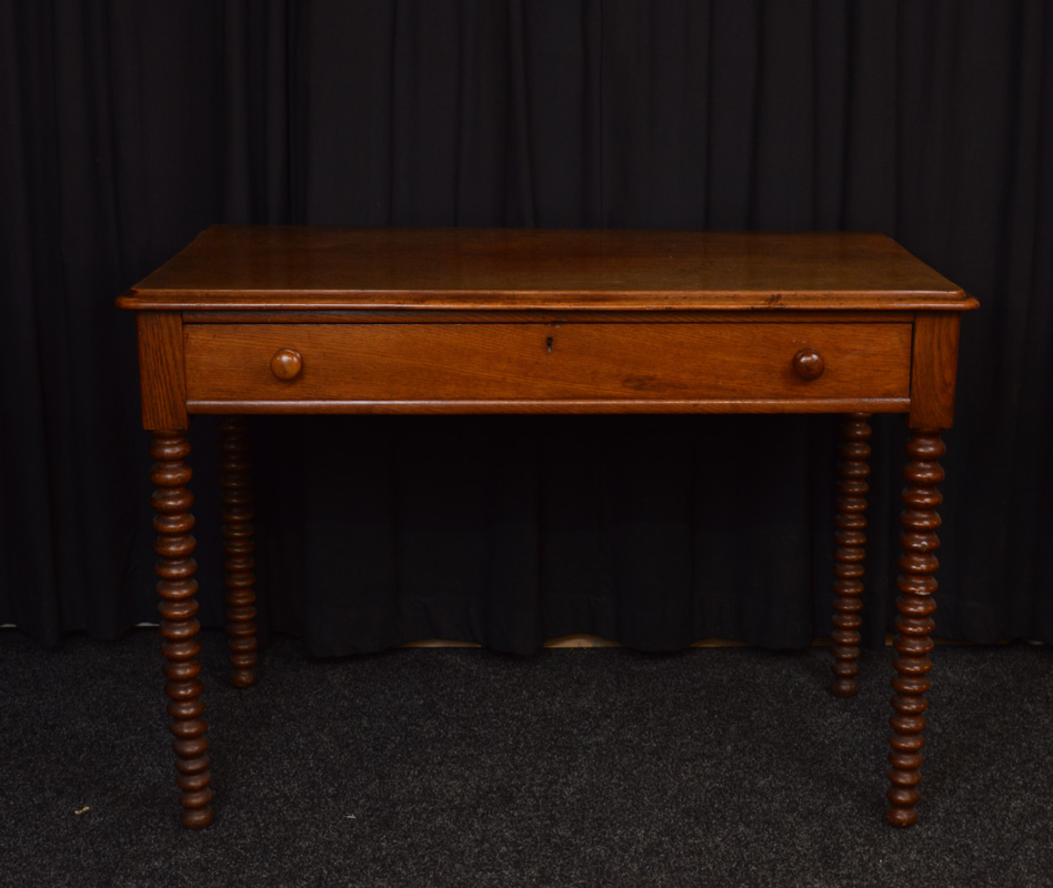 An oak rectangular topped desk, having single long drawer with turned handles on bobbin supports,