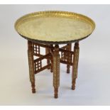 An Egyptian revival brass tray top table, with folding wooden stand with inlaid panels to the