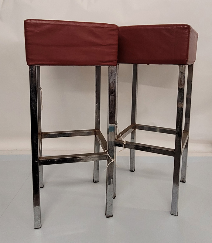 A pair of vintage stainless steel bar stools, rectangular form with red leather cushioned seats,