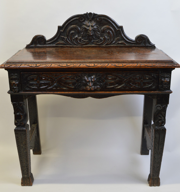 A heavily carved oak Green Man table, having figural carving to shaped back over rectangular top