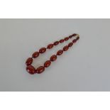 A string of knotted, graduated cherry "amber" beads, circa 1920, on a red silk cord with gilt