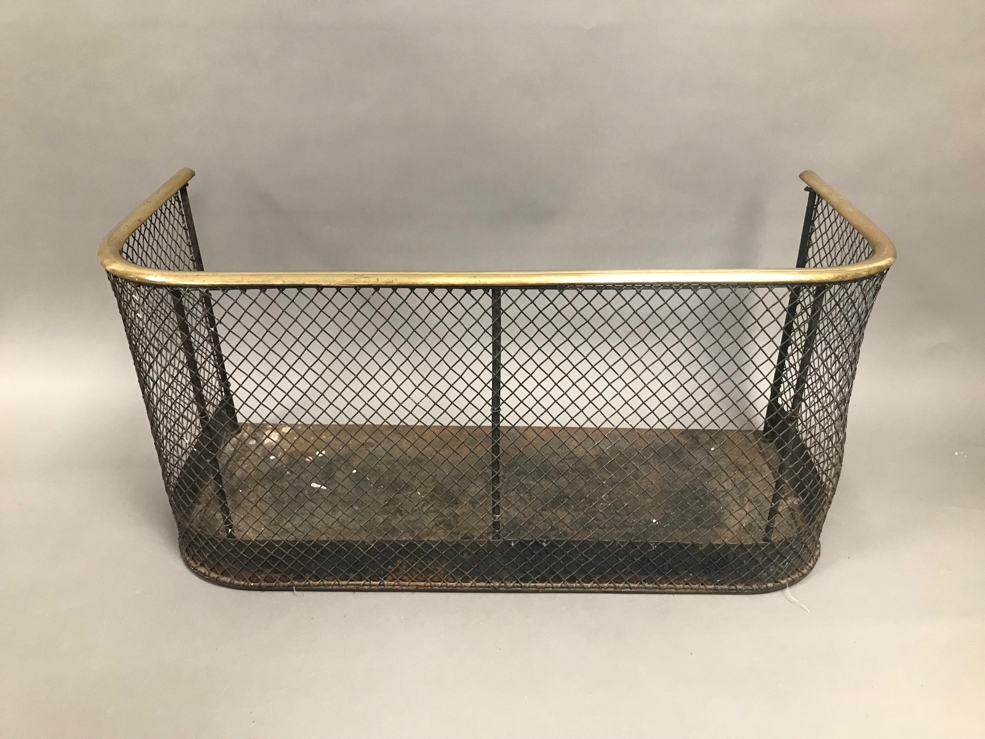 A Victorian iron and brass fire guard, 62cm wide, D shaped brass rail above mesh front