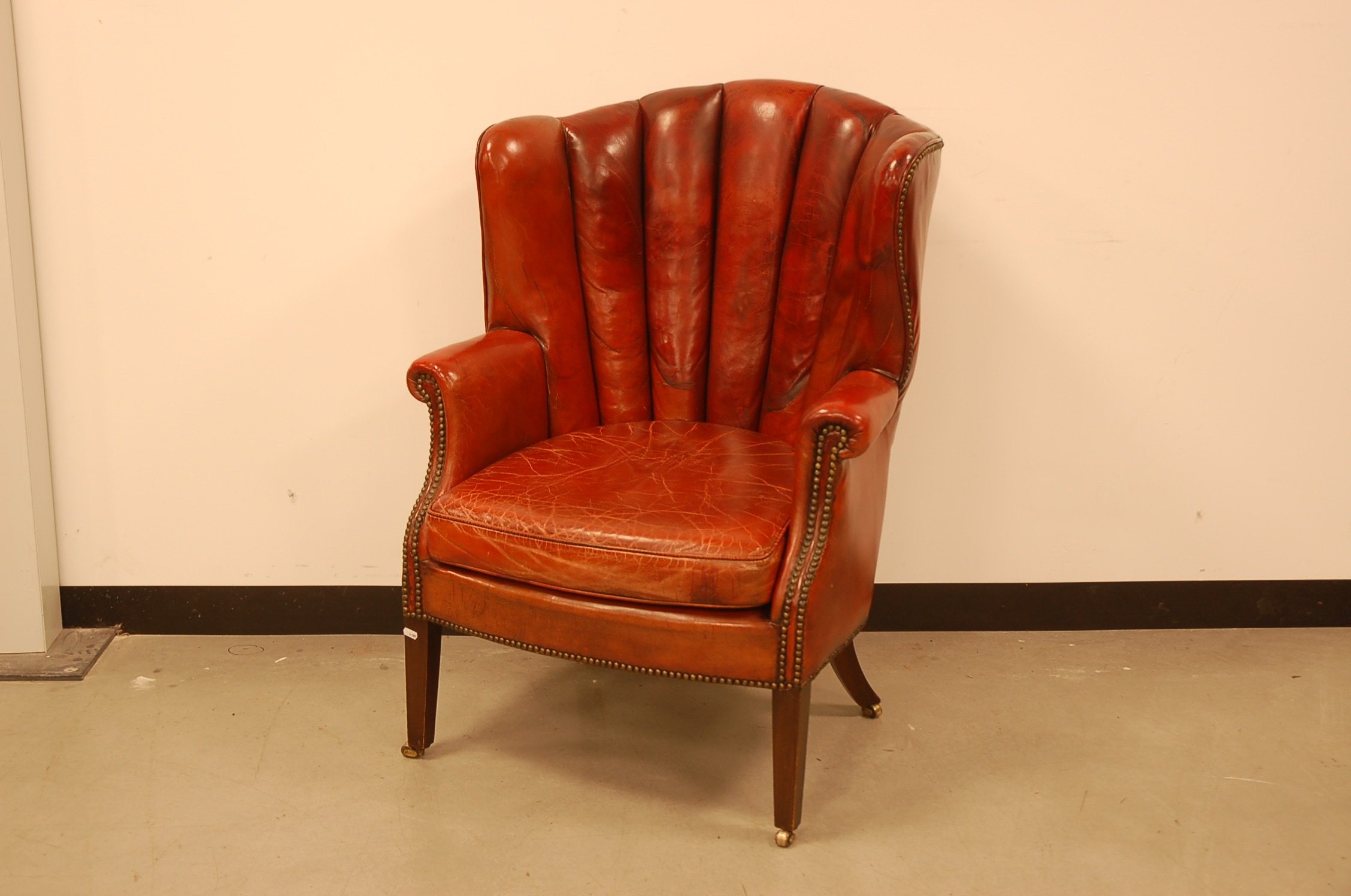 An early 20th century red leather armchair, on mahogany supports with brass casters