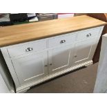 A modern white band light oak cabinet with a rectangular top above three drawers with cupboards unde