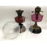 Two oil lamps comprising one with a cranberry glass reservoir plus one other.