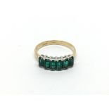 A Continental gold ring set with a row of green st