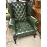 A Green leather button down back and seat wing arm chair.