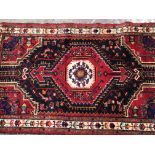 A hand knotted Middle Eastern wool rug with a central medallion on a red field. 145cm x90cm