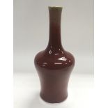 A red glazed ceramic vase with an elongated neck,