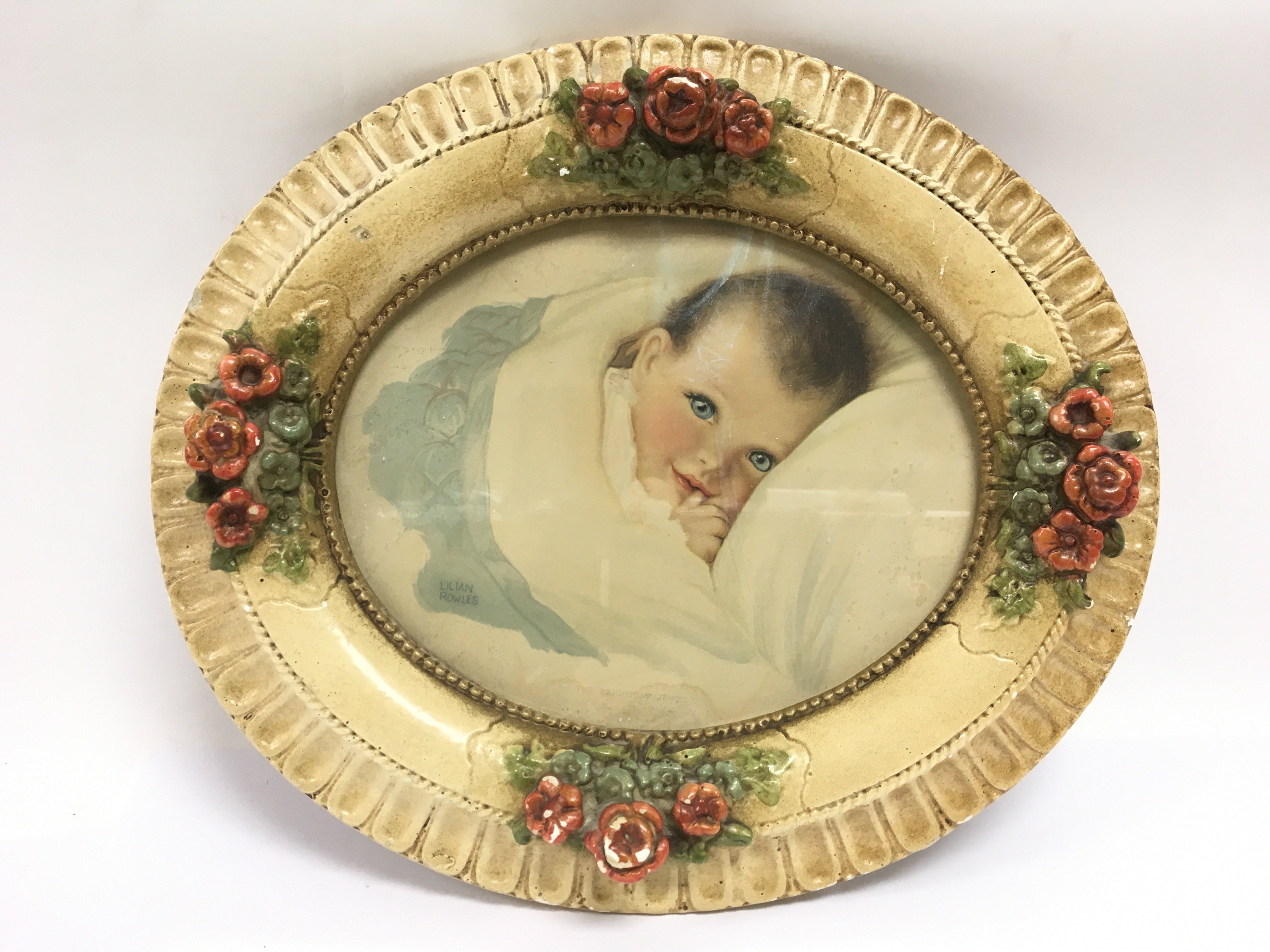 A Lilian Rowles print of an infant housed in a plaster oval shaped frame.