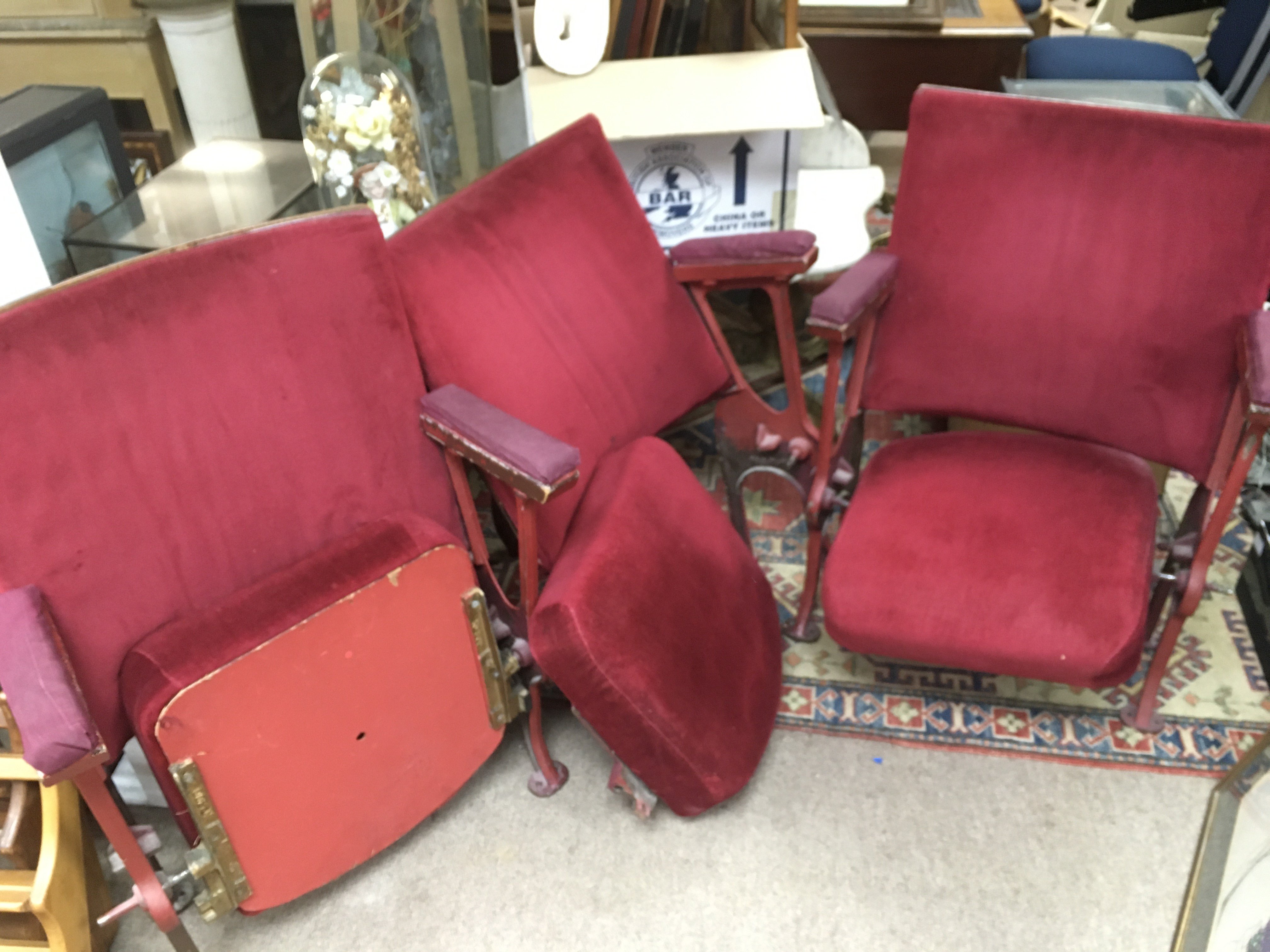 Three old cinema seats with red fabric upholstery.