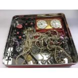 A tin of costume jewellery including a vintage Garrard folding travelling alarm clock.