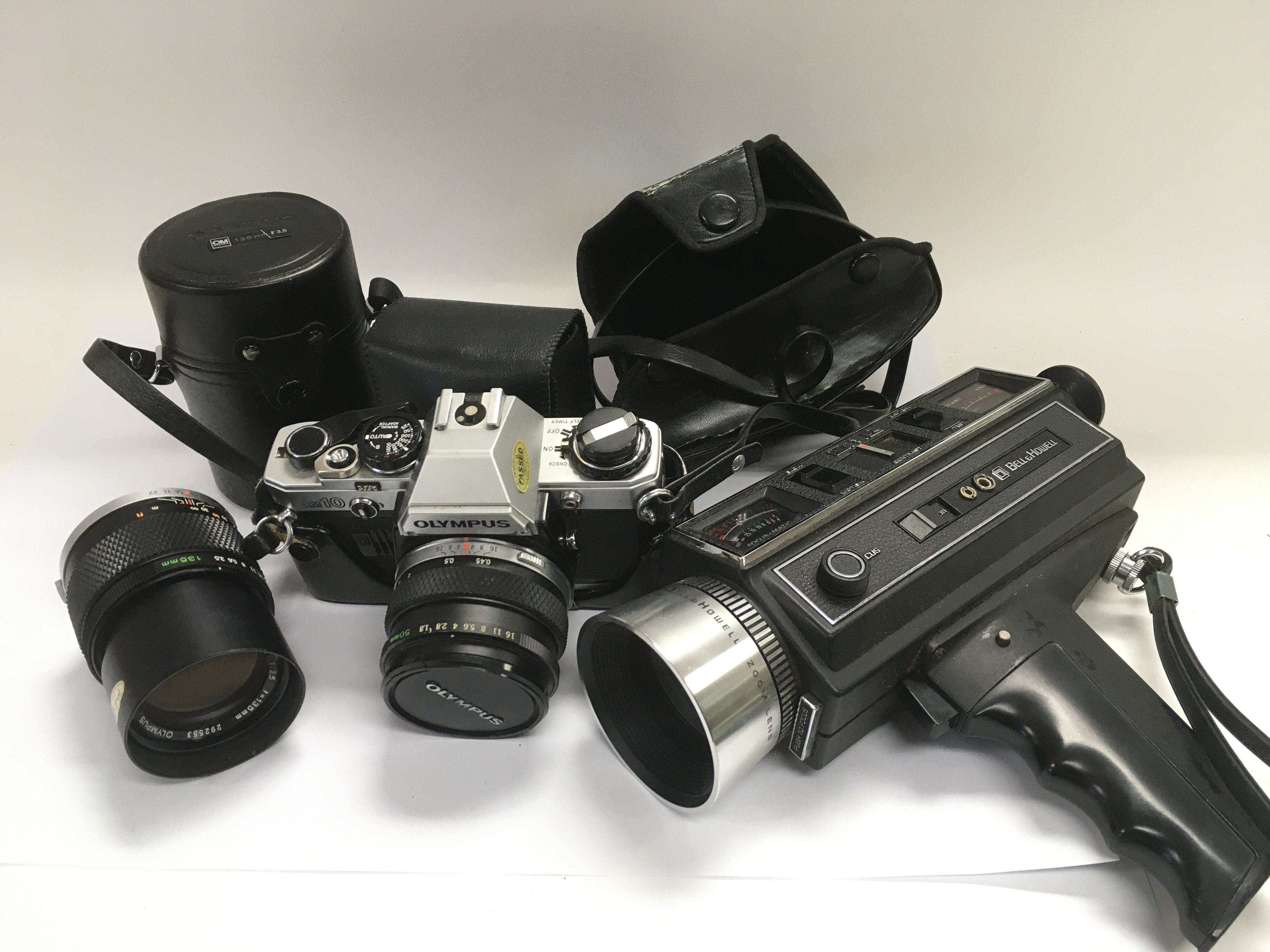 An Olympus camera and lenses plus a vintage Bell & Howell autoload 1216 camcorder with zoom lens.