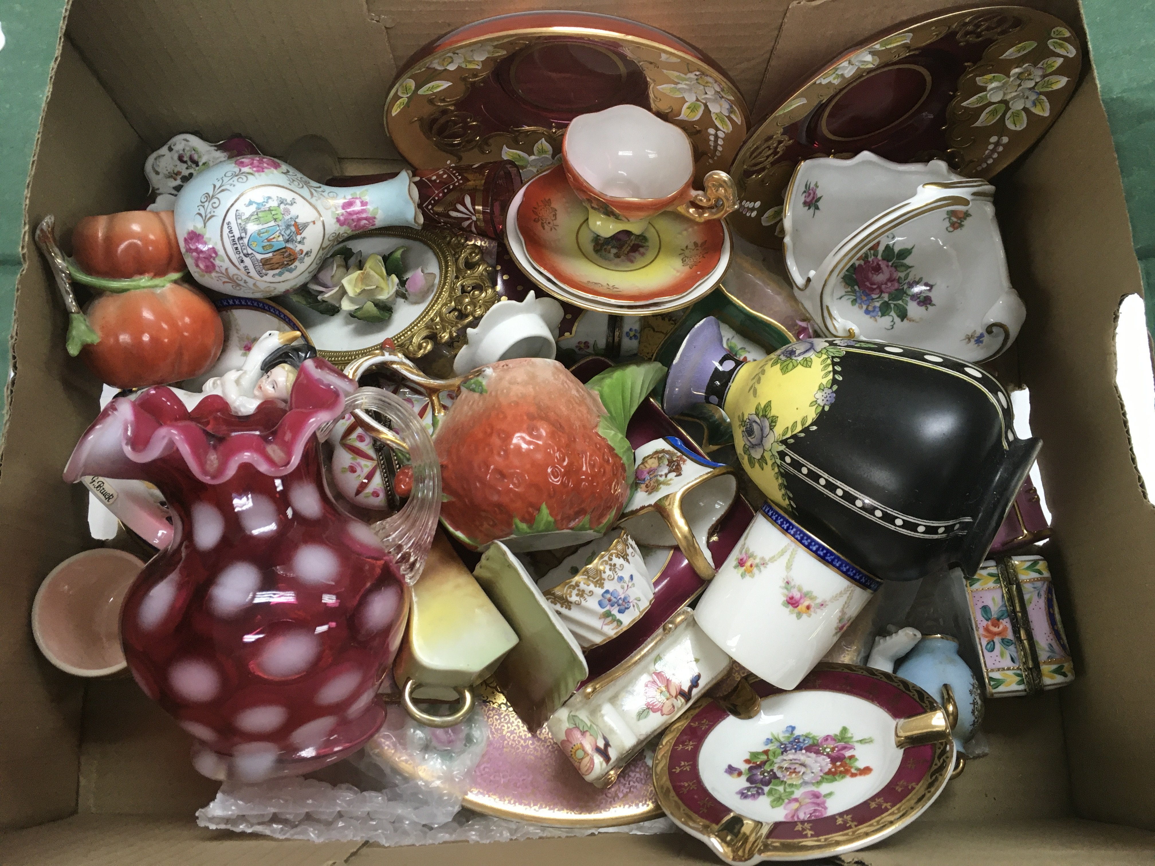 A box of glassware and ceramic items including a cranberry jug, crested ware bud vase of Southend