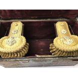 A cased tin containing a pair of epaulettes