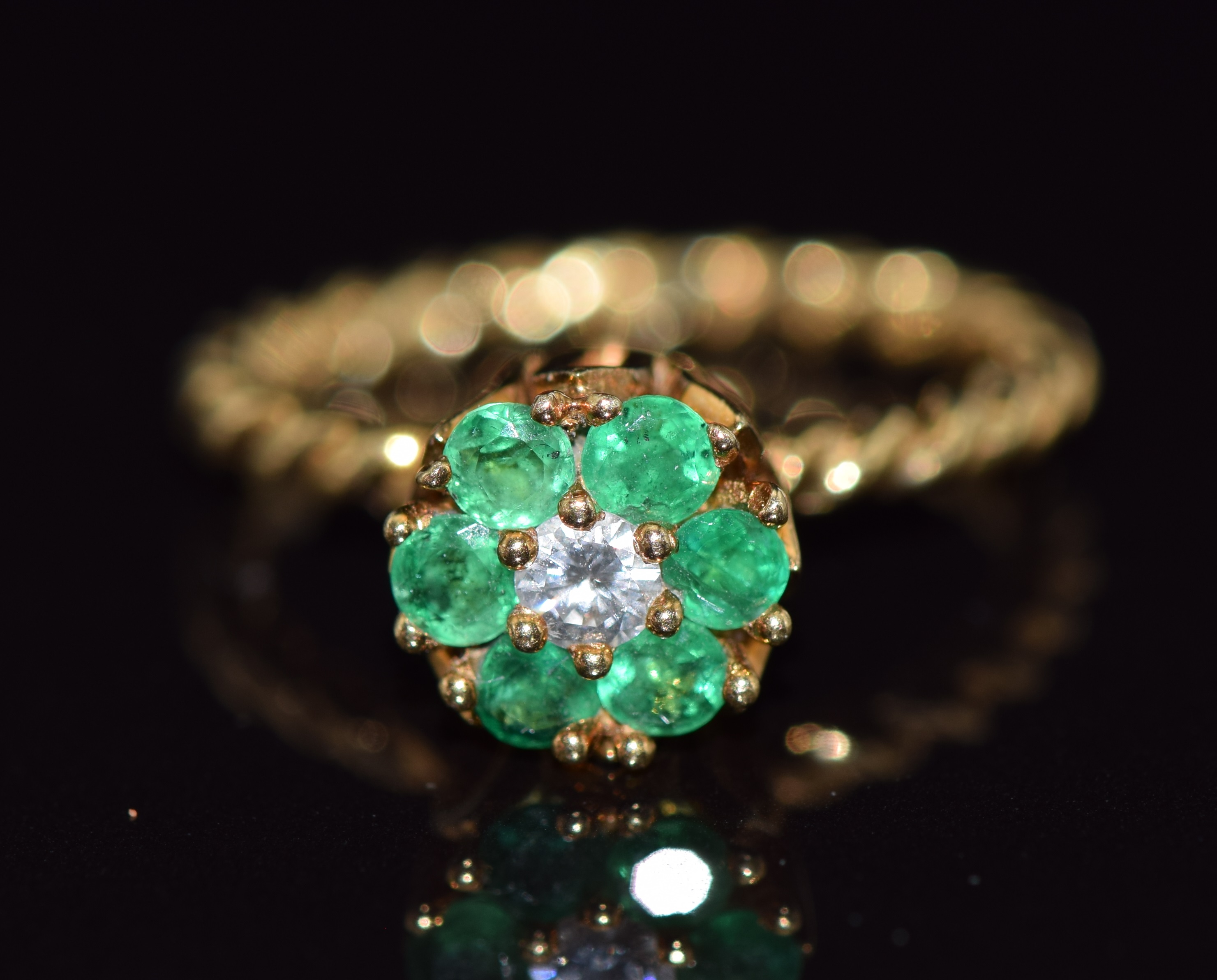 An 18ct gold ring set with a round cut diamond surrounded by emeralds on a rope twist band, 3.6g,