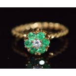 An 18ct gold ring set with a round cut diamond surrounded by emeralds on a rope twist band, 3.6g,