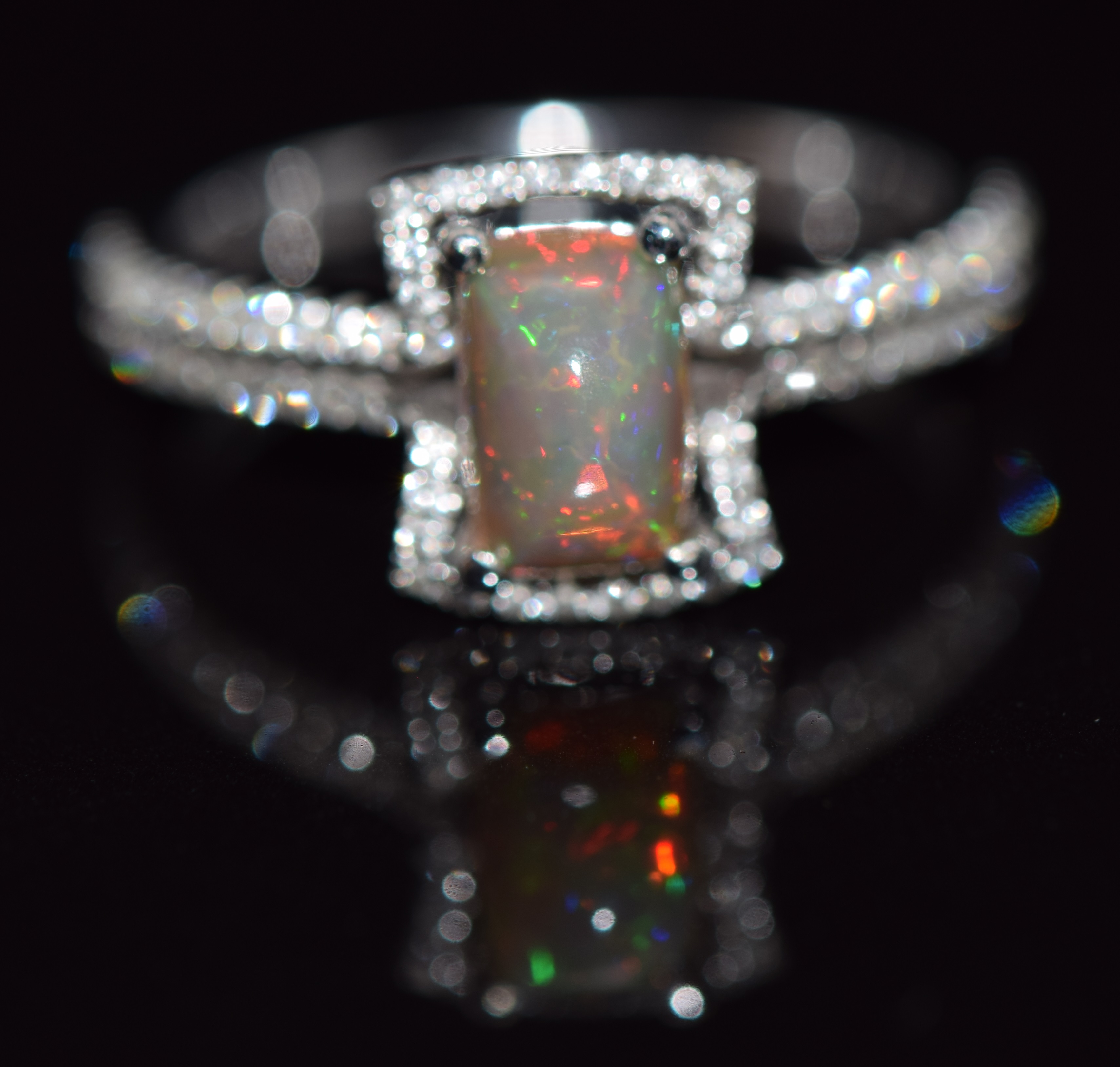 An 18ct white gold ring set with an Australian opal surrounded by diamonds and with further diamonds