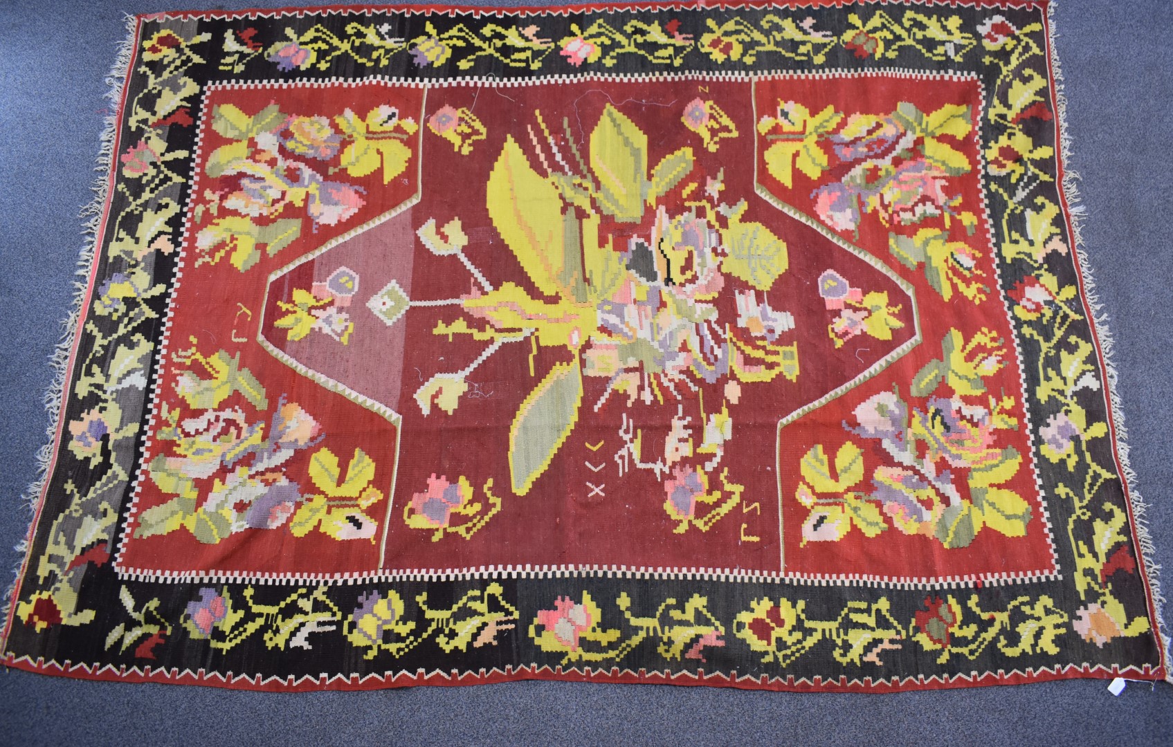 A large rug with central abstract yellow motif on a wine ground, within a black border and floral