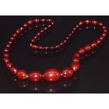 A cherry amber necklace made up of 53 graduated oval beads, 64g, largest bead 2.1 x 3cm