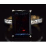 A 9k gold ring set with an emerald cut garnet and a diamond to each shoulder, 6.2g, size N