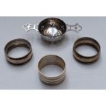 Three hallmarked silver napkin rings and a hallmarked silver tea strainer, width 11.5cm, weight 88g