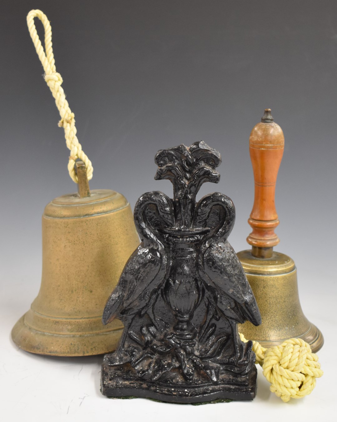 Brass hand bell, hanging bell and a cast iron door porter with bird decoration and impressed 'Cannon