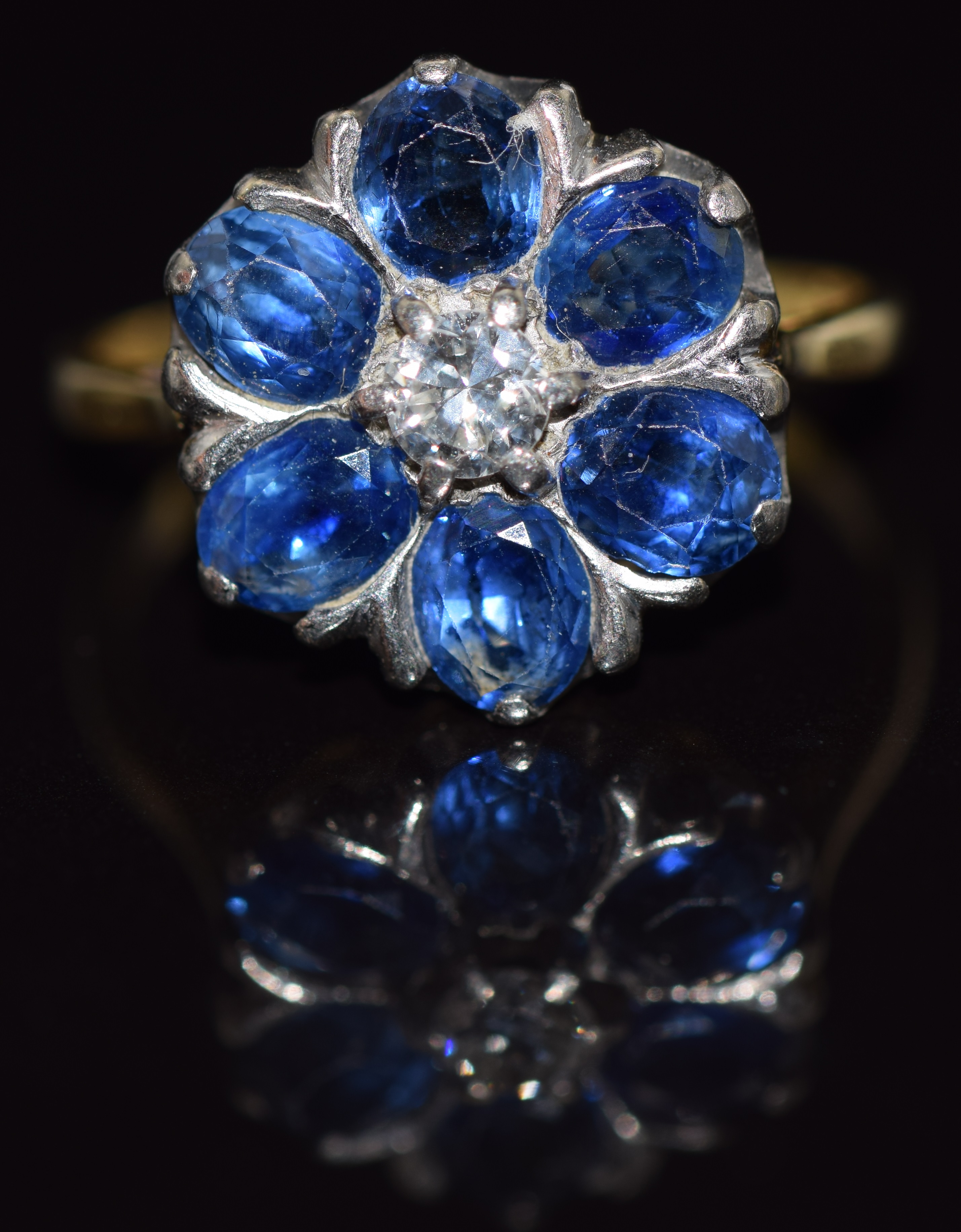 An 18ct gold ring set with a diamond surrounded by oval cut sapphires, each approximately 0.3cts,