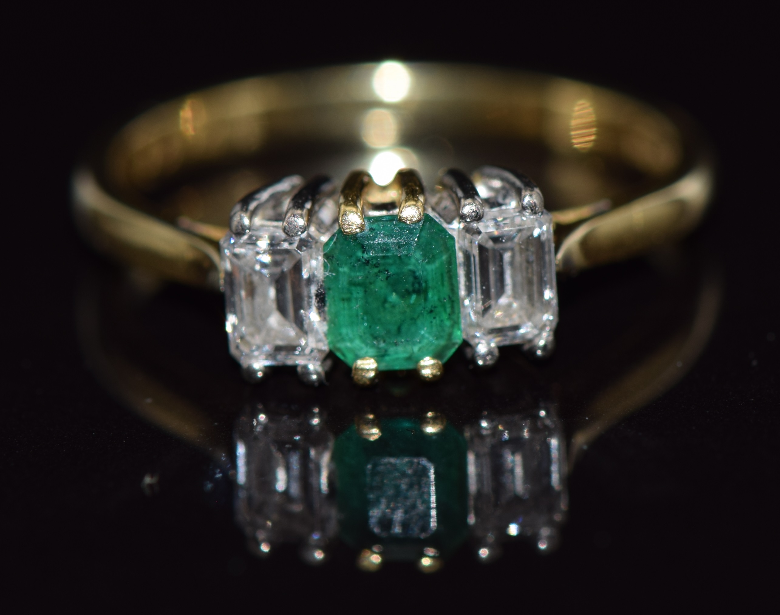 An 18ct gold ring set with an emerald cut emerald and two emerald cut diamonds, approximate