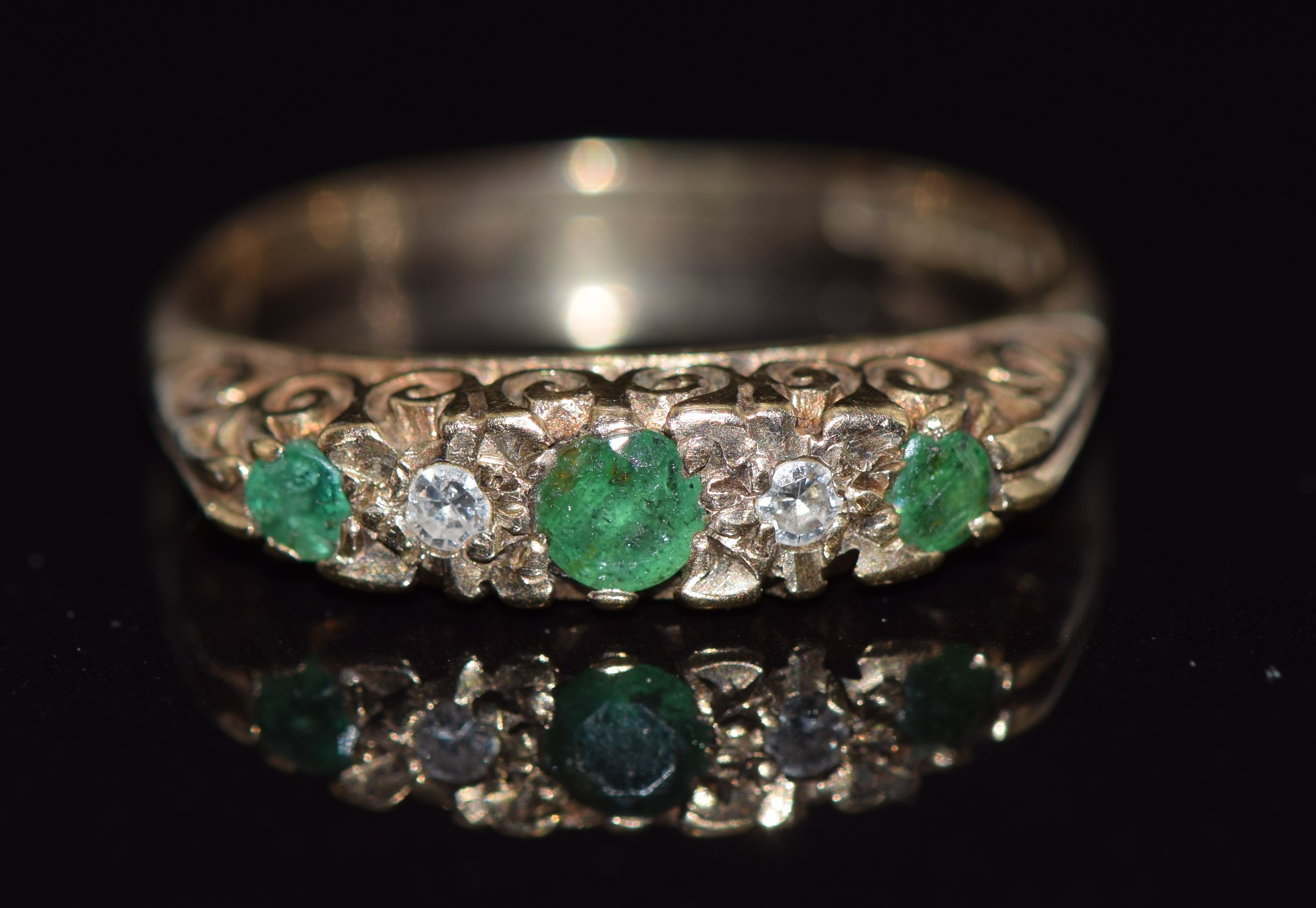 A 9ct gold ring set with round cut emeralds and diamonds in a scrolling setting, 2.4g, size M