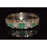 A 9ct gold ring set with round cut emeralds and diamonds in a scrolling setting, 2.4g, size M