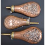 Three copper and brass powder flasks, two with embossed decoration of a cannon, guns and flags the