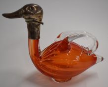 A pedestal glass figural duck claret jug with white metal mount, the hinged duck head folding back