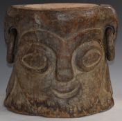 A carved hardwood tribal stool with facial decoration and twin loop earring handles, H29 x D29cm