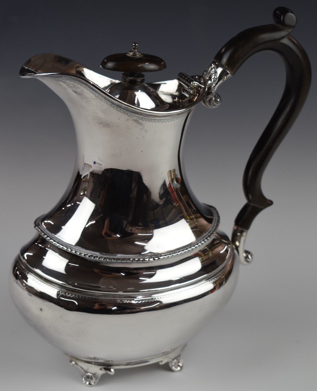 Edward VII hallmarked silver hot water jug with stained wood handle, raised on four feet, London