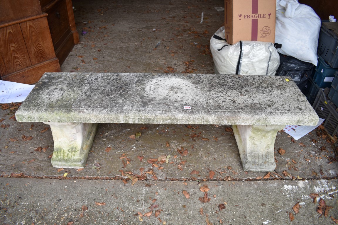 A reconstituted stone garden bench, having a pair of pedestal supports, 141cm wide.