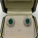 A PAIR OF 18CT WHITE GOLD STUD EARRINGS central set with oval 1.66ct emeralds surrounded by .80ct