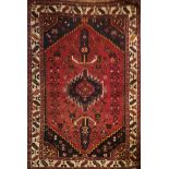 A IRANIAN SHIRAZ WOOLLEN RUG With stylised lozenges on a red ground. (138cm x 231cm)