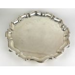 AN EARLY 20TH CENTURY SILVER SALVER TRAY Having a scalloped edge and raised on three scroll feet,
