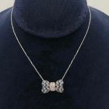 AN 18CT WHITE GOLD BOW FORMED PENDANT set with diamonds and sapphires, on chain 1.7cm