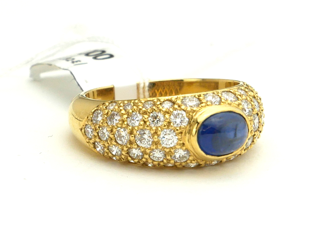 AN 18CT GOLD, CABOCHON CUT SAPPHIRE AND DIAMOND RING The sapphire flanked by diamond encrusted