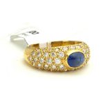 AN 18CT GOLD, CABOCHON CUT SAPPHIRE AND DIAMOND RING The sapphire flanked by diamond encrusted