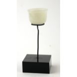 A CARVED INDIAN JADE MINIATURE BOWL Spherical form with fluted base, on black perspex stand. (approx